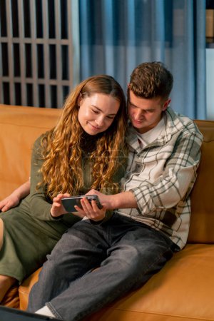 Photo for Young couple in love on a yellow sofa hugging and flirting reading the news on the phone - Royalty Free Image