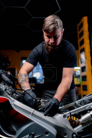 Dans un atelier de réparation de motos, un maître s'occupe du câblage du système moteur.