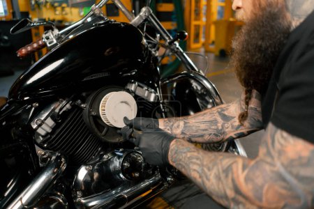 Dans un atelier de réparation de motos, un mécanicien sort un filtre pour le remplacer par un nouveau