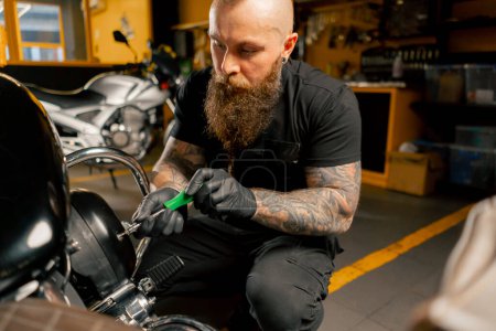 Dans un atelier de réparation de moto, un mécanicien dévisse les boulons sur le couvercle du filtre