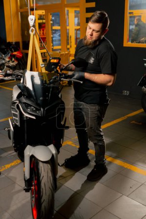 Dans un atelier de réparation de motos, un mécanicien relie une moto à un treuil aérien