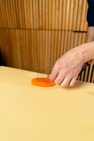 Téléchargez les photos : Gros plan dans un restaurant japonais un chef dans un uniforme bleu coupe le poisson pour les sushis en tranches sur un carton jaune - en image libre de droit