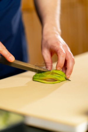 Photo for Close up in a Japanese restaurant chef in a blue uniform cuts avocado sushi into slices on a yellow board - Royalty Free Image