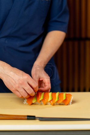 Photo for Close-up in a Japanese restaurant chef in a blue uniform on a yellow board spins a fish roll - Royalty Free Image