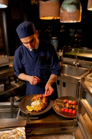Téléchargez les photos : Au restaurant japonais, le chef met des légumes frits dans une assiette comme plat d'accompagnement pour le poisson - en image libre de droit