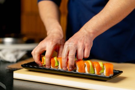 Foto de Primer plano en un restaurante japonés un chef en un uniforme azul pone sushi listo en un plato - Imagen libre de derechos