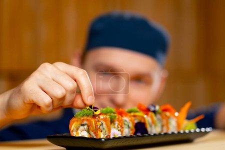 Foto de Primer plano en un chef de restaurante japonés en un uniforme azul decora sushi listo en un plato - Imagen libre de derechos