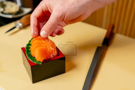 Téléchargez les photos : Gros plan dans un restaurant japonais le chef place des morceaux de poisson rouge sur un stand - en image libre de droit