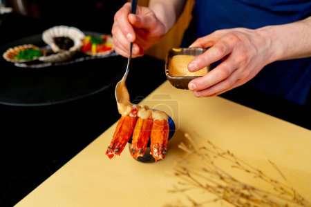 Foto de Primer plano en un restaurante japonés un chef en un uniforme azul vierte salsa sobre los camarones - Imagen libre de derechos