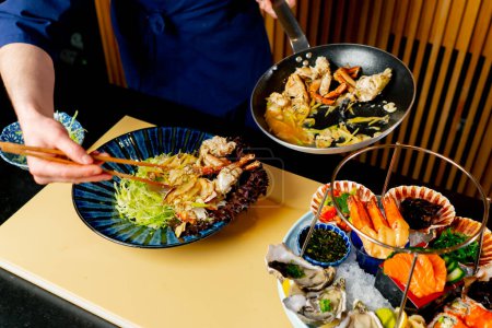 Photo for Close-up in a Japanese restaurant a chef in blue prepares an expensive plate of seafood - Royalty Free Image