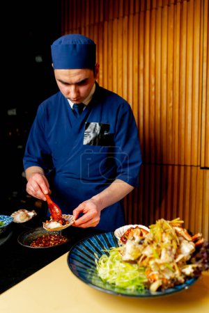 Téléchargez les photos : Dans un restaurant japonais un chef en bleu prépare une assiette chère de fruits de mer - en image libre de droit