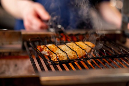 Téléchargez les photos : Fermer dans un restaurant japonais un chef dans un uniforme bleu frites poisson sur le gril dans la cuisine - en image libre de droit