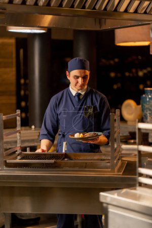 Photo for In Japanese restaurant a chef in a blue uniform stands with a prepared dish in his hand - Royalty Free Image