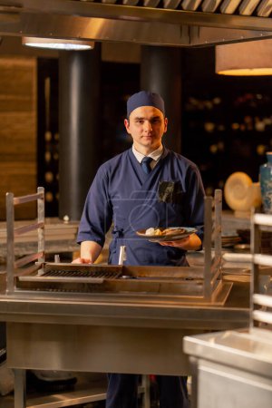 Téléchargez les photos : Au restaurant japonais un chef en uniforme bleu se tient debout avec un plat préparé à la main - en image libre de droit