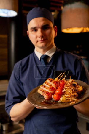 Photo for Close-up in a Japanese restaurant a chef in a blue uniform stands with a prepared dish in his hand - Royalty Free Image