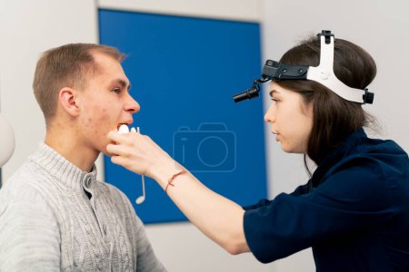 Foto de Primer plano en la clínica un médico joven oído garganta nariz examina la garganta del paciente - Imagen libre de derechos