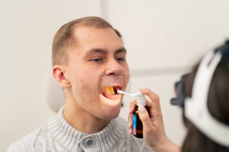 Téléchargez les photos : Gros plan dans la clinique médecin oreille gorge nez vaporise analgésique dans la gorge des patients - en image libre de droit