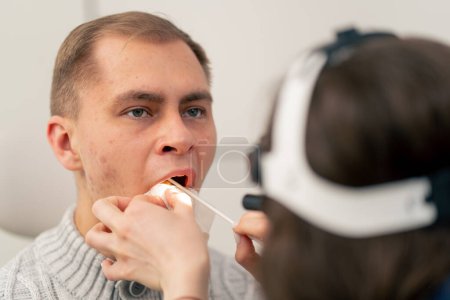 Foto de Primer plano en la clínica un médico joven oído garganta nariz examina la garganta del paciente - Imagen libre de derechos