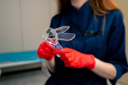 Téléchargez les photos : Gros plan dans un cabinet gynécologique un gynécologue médecin en gants rouges tient un miroir gynécologique - en image libre de droit