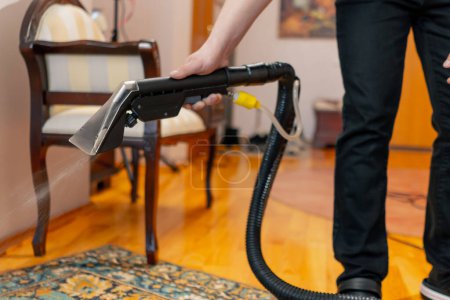 Foto de En el apartamento maestro de limpieza riega la alfombra con detergente de una aspiradora profesional - Imagen libre de derechos