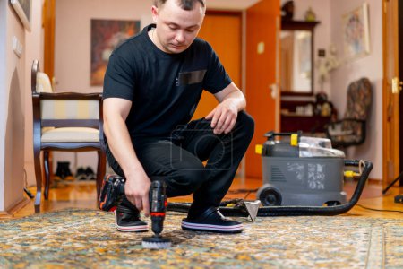 Foto de En el apartamento un limpiador maestro limpia la alfombra con detergente usando un destornillador y un cepillo - Imagen libre de derechos