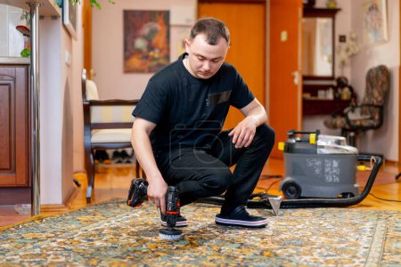 Foto de En el apartamento un limpiador maestro limpia la alfombra con detergente usando un destornillador y un cepillo - Imagen libre de derechos