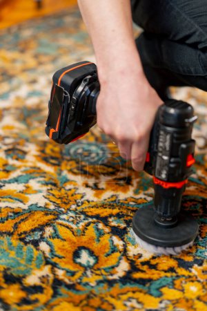 Foto de Primer plano en el apartamento un limpiador maestro limpia la alfombra con detergente utilizando un destornillador y un cepillo - Imagen libre de derechos