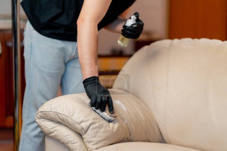 Photo for Professional cleaning of an apartment a cleaner polishes a leather sofa with polish - Royalty Free Image