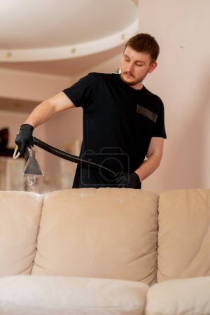 Téléchargez les photos : Nettoyage professionnel dans un appartement un nettoyeur mouille un canapé textile avant de laver - en image libre de droit