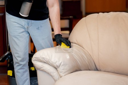 Téléchargez les photos : Fermer nettoyage professionnel dans un appartement un nettoyeur applique un agent de polissage sur un canapé en cuir - en image libre de droit