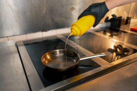Téléchargez les photos : Dans une cuisine professionnelle, le chef verse de l'huile dans une petite poêle sur la cuisinière - en image libre de droit