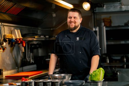 Foto de En un retrato de cocina profesional de un chef con una chaqueta negra en la cocina sonrisa feliz - Imagen libre de derechos