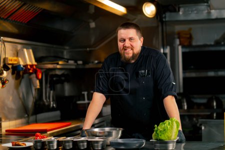 Photo for In a professional kitchen portrait of a chef in a black jacket in the kitchen happy smile - Royalty Free Image