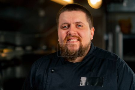 Téléchargez les photos : Gros plan dans un portrait professionnel de cuisine d'un chef en veste noire dans la cuisine sourire heureux - en image libre de droit
