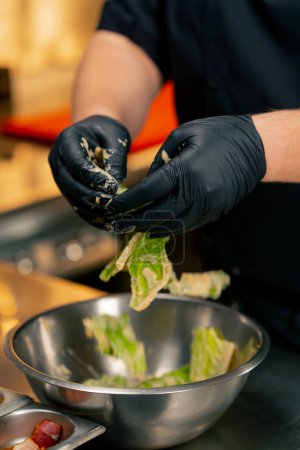 Photo for Close-up in a professional kitchen the chef mixes lettuce leaves with sauce with his hands - Royalty Free Image