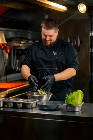 Téléchargez les photos : Dans une cuisine professionnelle, le chef mélange des feuilles de laitue avec de la sauce avec ses mains - en image libre de droit