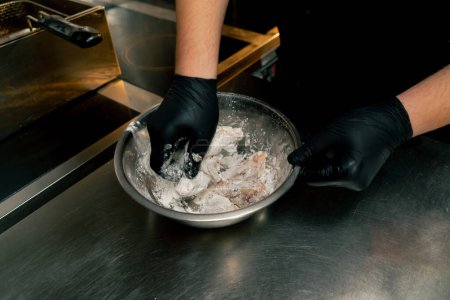 Téléchargez les photos : Close-up dans une cuisine professionnelle le chef mélange des ailes de poulet dans de la farine - en image libre de droit