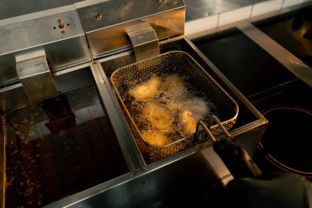 Foto de Primer plano en una cocina profesional freír las alas de pollo en aceite en una freidora - Imagen libre de derechos