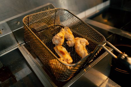 Foto de Primer plano en una cocina profesional el chef comprueba la preparación de las alas de pollo en la freidora - Imagen libre de derechos