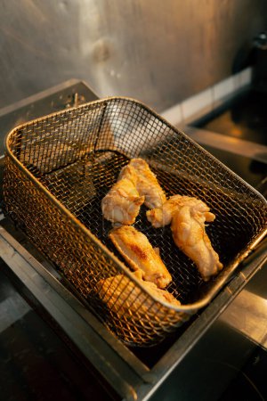 Foto de Primer plano en una cocina profesional el chef comprueba la preparación de las alas de pollo en la freidora - Imagen libre de derechos