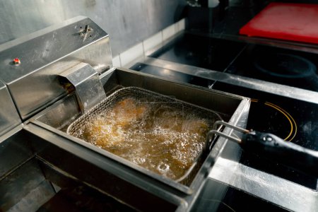 Téléchargez les photos : Close-up dans une cuisine professionnelle friture ailes de poulet dans l'huile dans une friteuse - en image libre de droit