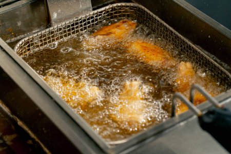 Foto de Primer plano en una cocina profesional freír las alas de pollo en aceite en una freidora - Imagen libre de derechos