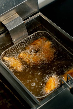 Téléchargez les photos : Close-up dans une cuisine professionnelle friture ailes de poulet dans l'huile dans une friteuse - en image libre de droit