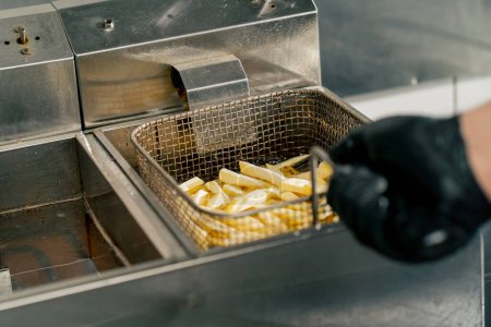 Foto de Primer plano en una cocina profesional el chef pone papas fritas en aceite en la freidora - Imagen libre de derechos