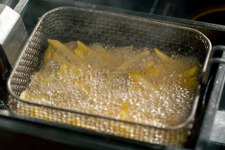 Foto de Primer plano en una cocina profesional freír papas fritas en aceite en una freidora - Imagen libre de derechos