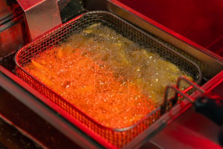 Foto de Primer plano en una cocina profesional freír papas fritas en aceite en una luz roja freidora - Imagen libre de derechos