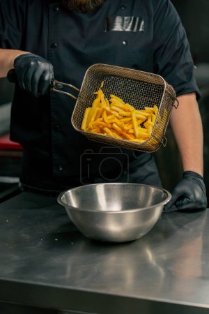 Foto de Primer plano en una cocina profesional el chef vierte papas fritas en un recipiente de hierro - Imagen libre de derechos