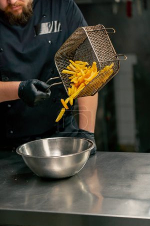 Téléchargez les photos : Gros plan dans une cuisine professionnelle le chef verse des frites dans un bol de fer - en image libre de droit