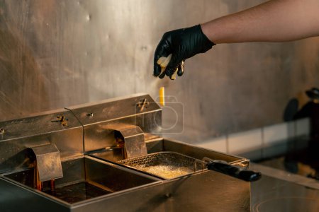 Foto de Primer plano en una cocina profesional, el chef lanza papas fritas en la freidora - Imagen libre de derechos