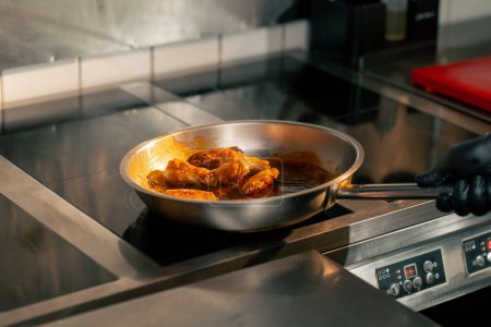 Foto de Primer plano de las alas de pollo fritas en salsa en una sartén en una cocina profesional - Imagen libre de derechos